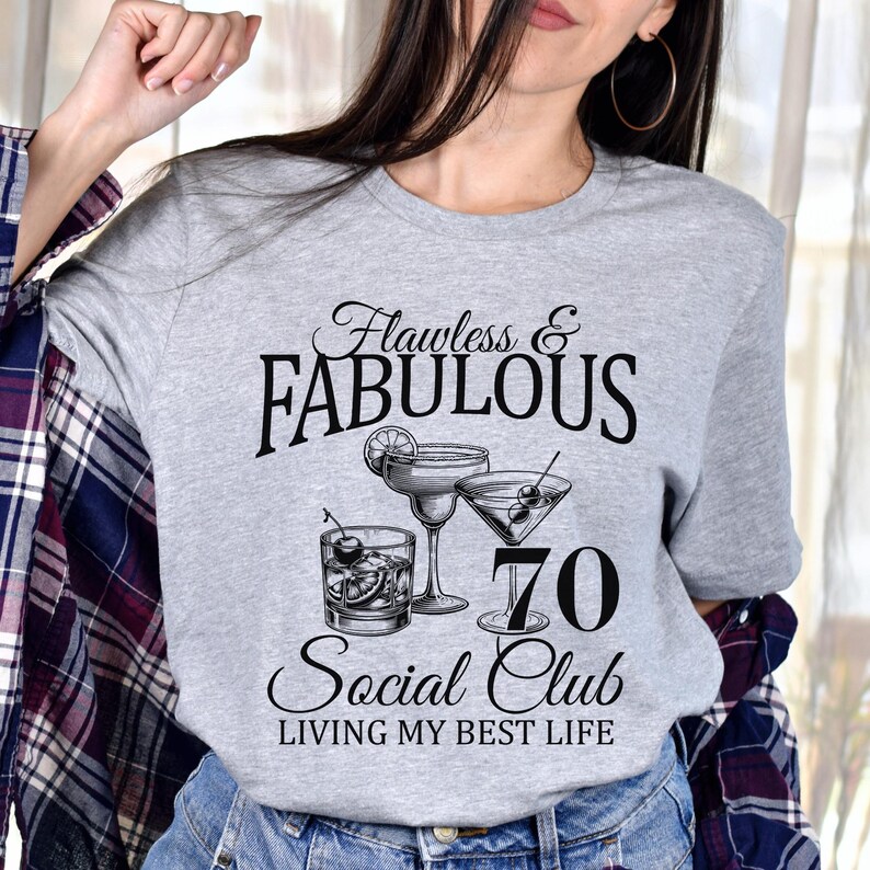 May include: A gray t-shirt with the words "Flawless & Fabulous" above the number "70" and the words "Social Club" and "Living My Best Life". The shirt features illustrations of cocktails.