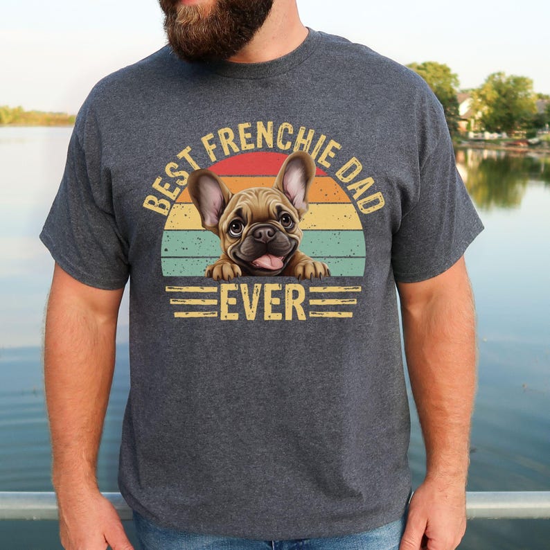 May include: A dark gray t-shirt with a vintage-style graphic of a French bulldog peeking over a retro sunset. The text "Best Frenchie Dad Ever" is printed in white on the shirt.