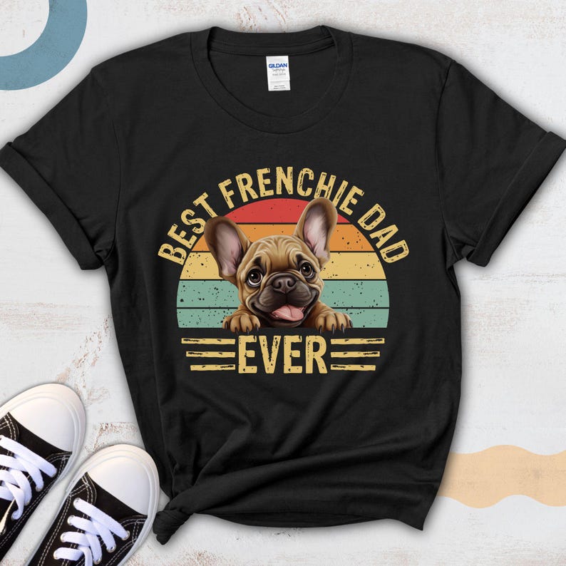 May include: Black t-shirt with a vintage-style graphic of a French Bulldog peeking over a retro sunset. The text reads "Best Frenchie Dad Ever".