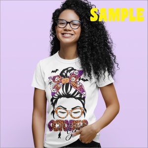 May include: White t-shirt with a graphic of a woman with a messy bun, wearing glasses and a purple and orange bow with Halloween-themed patterns. The text "October Girl" is below the graphic.