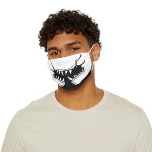 May include: White face mask with a black graphic design of a monster's mouth and teeth. The mask has white ear loops and is worn by a person.