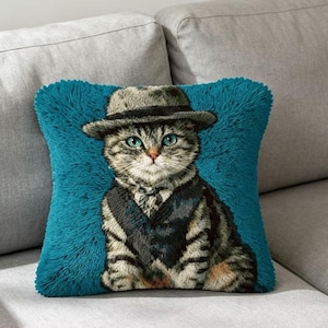 Peut inclure: Un coussin carré avec un fond texturé à poils longs de couleur bleu sarcelle vif. Au centre, une image tissée détaillée représente un chat tigré portant un chapeau fedora gris et un gilet sombre. Le chat a des yeux bleus et un pelage gris et brun.