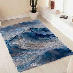 Könnte beinhalten: Ein rechteckiger Teppich mit einem Wellenmuster in Blau- und Grautönen. Der Teppich hat eine strukturierte Oberfläche, wobei das Wellenmuster prominent in der Mitte dargestellt wird. Das Design erinnert an das Meer.