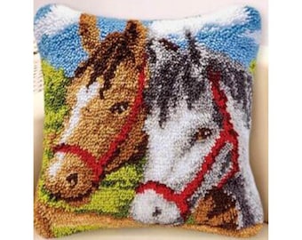 May include: A colorful rug hooking kit featuring two horses' heads, one brown and one white, with red bridles. The horses are set against a green grassy background with a blue sky.