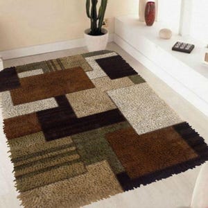May include: A brown, beige, green and black area rug with a geometric pattern. The rug has a shaggy texture.