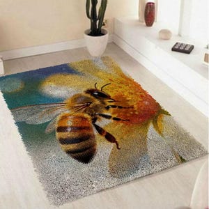 May include: A rectangular rug featuring a detailed image of a bee on a yellow flower. The bee has brown and black stripes, with a detailed wing structure. The rug has a textured appearance and is placed on a light-colored floor.
