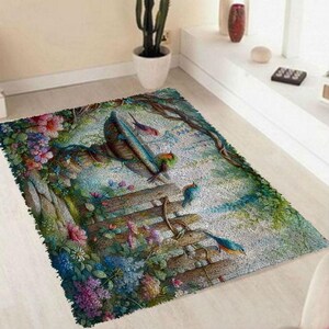 Op de afbeelding: Een rechthoekig vloerkleed met een gedetailleerde geweven scène van een houten tuinbank omringd door kleurrijke bloemen, waaronder roze, paarse en blauwe bloesems, met verschillende kleine vogels op de bank en op de takken.