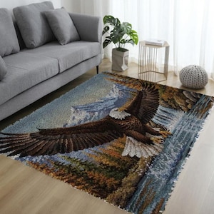 May include: A rectangular area rug featuring a detailed woven scene of a bald eagle in flight with wings fully spread. The design includes a mountain landscape, a flowing waterfall, and a forest with brown, blue, and green tones throughout.