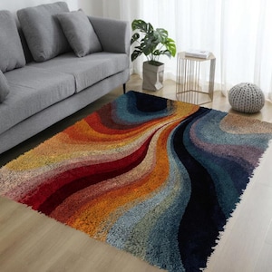 May include: A colorful area rug with a wavy design. The rug features a blend of warm and cool tones, including red, orange, yellow, blue, and black. The rug is placed on a wooden floor in a living room setting.