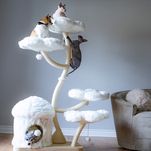 Puede incluir: Un árbol para gatos blanco con múltiples plataformas con forma de nubes. El árbol para gatos tiene un poste para rascar y una guarida acogedora. Tres gatos están jugando en el árbol para gatos.