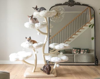 May include: A white cat tree with multiple platforms shaped like clouds. The cat tree has a brown wooden base and is decorated with white pom-poms. Four cats are sitting on the platforms, and a fifth cat is sitting on the base of the tree.