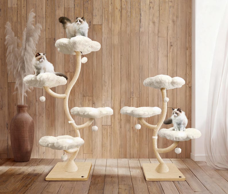 May include: Two cat trees with cloud-shaped platforms and beige posts. Each tree has multiple levels, with fluffy white platforms and small dangling balls. Several cats with fluffy white and brown fur are perched on the platforms.