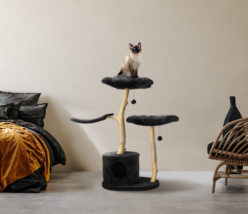May include: A black cat tree with three platforms and a scratching post. The platforms are covered in soft, black fabric and the post is made of natural wood. A cat is sitting on the top platform.