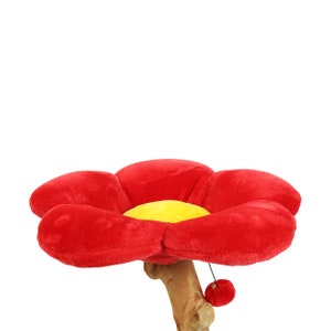 May include: Red plush flower-shaped cat bed with a yellow center and a dangling red toy. The bed is attached to a wooden branch.