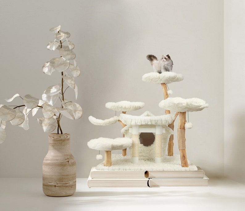 May include: White cat tree with multiple platforms and a house. The cat tree is made of wood and has a fluffy white covering. The cat tree is on a white surface with a white vase and a leafy plant.