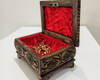 May include: A wooden box with intricate carvings and a red velvet interior. The box is open and a gold necklace is inside.
