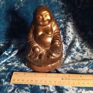 May include: A small, gold-coloured ceramic statue of a smiling Buddha sitting in a meditative pose. The statue is about 15 cm tall and has a round base.