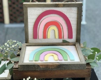 May include: Two wooden signs with rainbow designs. The top sign features a red, pink, orange, and yellow rainbow. The bottom sign features a green, pink, and yellow rainbow.
