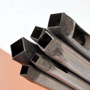 May include: A collection of metal square hole punches of varying sizes. The punches are made of a silver-colored metal and have a square cutting edge. The tools are held together, with the square ends facing the viewer.