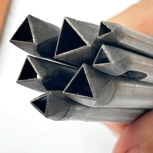 Könnte beinhalten: Nahaufnahme eines Bündels metallischer, dreieckiger Lederwerkzeuge. Die Werkzeuge sind silberfarben und haben eine hohle, dreieckige Öffnung. Die Werkzeuge werden in einer Hand gehalten, mit einer braunen Lederoberfläche im Hintergrund.