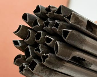 Könnte beinhalten: Eine Sammlung von Metall-Formstempeln, darunter Herzen, Sterne, Quadrate und Dreiecke. Die Stempel sind aus dunklem Metall gefertigt und in einem Bündel angeordnet. Der Hintergrund ist hellorange.
