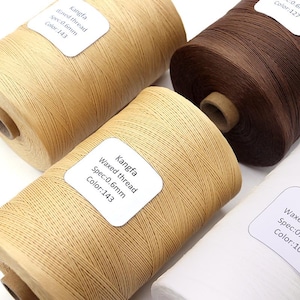 May include: Close-up of four spools of waxed thread in various colors: tan, brown, and white. Each spool has a label that reads "Kangfa Waxed thread Spec:0.6mm Color:143". The thread is tightly wound, suggesting a durable material.