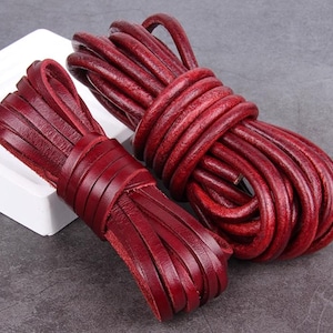 May include: Two bundles of burgundy leather cord. One bundle is coiled, and the other is cut into strips and neatly arranged. The leather has a rich, textured appearance, suggesting high quality and durability. The cords are suitable for crafting.