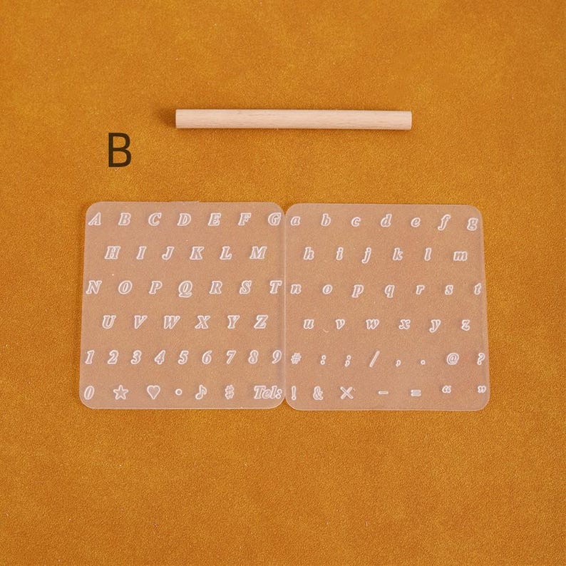 May include: A clear, flexible alphabet and number stencil set with uppercase and lowercase letters, numbers, and symbols. A small wooden dowel is above the stencil. The letter "B" is in the upper left corner.