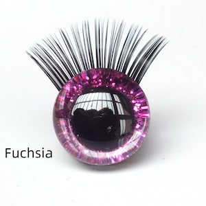May include: A fuchsia-colored, glitter-infused glass eye with black eyelashes. The eye has a reflective surface and the word "Fuchsia" is printed below it. This item is likely for crafting or doll-making.