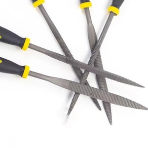 May include: A set of four metal files with textured grey steel blades and black handles featuring yellow accents. The tools are arranged in a fan-like pattern, showcasing the abrasive surfaces and the ergonomic grip design of each individual file.