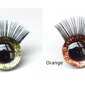 May include: Two decorative eye-shaped craft pieces. One is light green with black eyelashes, the other is orange with black eyelashes. The text "Light Green" and "Orange" are below each eye. These are likely for doll making or other crafts.