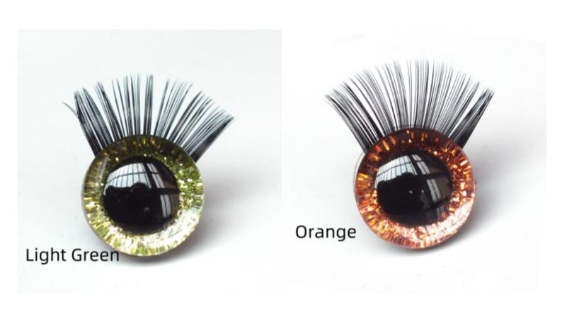 May include: Two decorative eye-shaped craft pieces. One is light green with black eyelashes, the other is orange with black eyelashes. The text "Light Green" and "Orange" are below each eye. These are likely for doll making or other crafts.
