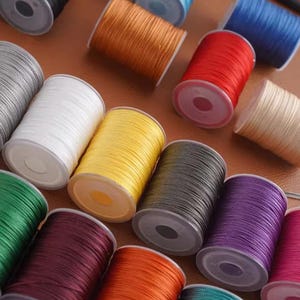 Könnte beinhalten: Eine Sammlung bunter Garnrollen in verschiedenen Farbtönen, darunter Schwarz, Weiß, Gelb, Rot und Blau. Die Rollen sind auf einer braunen Oberfläche angeordnet und zeigen die lebendigen Farben des Garns. Ideal für Bastel- und Nähprojekte.