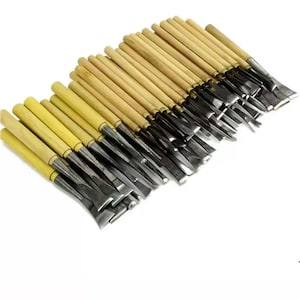 May include: A collection of wood carving chisels with wooden handles and metal blades. The chisels are arranged in a diagonal pattern, showcasing their sharp edges and varying blade shapes. The handles are light brown, and the blades are silver.