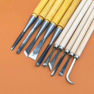 以下が含まれることがあります： 金属製の刃と木製の柄を持つ9本の木彫り用工具セット。様々な形状のノミ、彫刻刀、そして湾曲したフックツールが含まれており、すべて研磨されたスチール製の先端と滑らかな木製の軸を備えています。