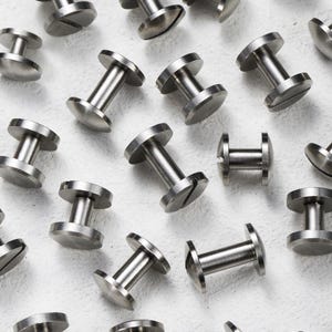 May include: A collection of small, silver metal rivets. Each rivet features a flat, circular head at either end, joined by a cylindrical shaft. Some rivets have a slotted head for a screwdriver. Metric measurements.