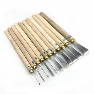 Puede incluir: Un juego de herramientas para tallar madera con mangos de madera y hojas de metal. Cada herramienta está numerada con tinta azul. Las hojas tienen varias formas y tamaños, adecuadas para proyectos de carpintería detallados.