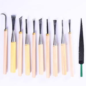 Puede incluir: Un conjunto de herramientas para tallar madera, que incluye varios cinceles y una escofina. Las herramientas tienen mangos de madera y hojas de metal, dispuestas sobre un fondo blanco. La escofina tiene una superficie negra y un mango verde.
