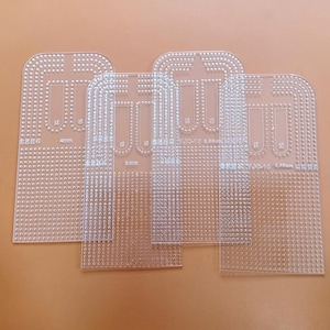 Peut inclure: Plusieurs gabarits de loisirs créatifs en plastique transparent, percés de petits trous. Chaque gabarit a une forme unique avec des bords arrondis et un motif central. Des mesures sont visibles, notamment 4 mm et 8 mm.