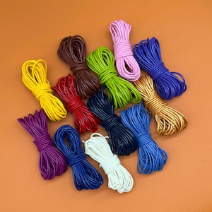 Può includere: Una collezione di tredici singoli fasci di cordino rotondo in vari colori solidi tra cui giallo, marrone, rosso, verde lime, rosa, blu scuro, bianco, viola, oro e sfumature di blu, ciascuno ordinatamente avvolto e fissato al centro.