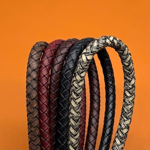 May include: A collection of six braided leather cords arranged in a row. The cords feature various colours and textures, including distressed brown, deep red, dark burgundy, solid black, and a black and white mottled pattern with a woven finish.