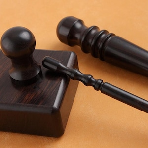 Könnte beinhalten: Ein Set dunkler brauner Holz-Schreibtischaccessoires, darunter ein Stempel mit quadratischer Basis und abgerundeter Oberseite, ein kleiner Stift und ein dekorativer Griff. Die Artikel sind auf einer hellbraunen Oberfläche angeordnet.