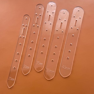 May include: Five clear acrylic watch strap templates with varying lengths, labeled 25mm, 30mm, 35mm, 38mm, and 40mm. Each template features a series of small holes and a central rectangular cutout for watch band hardware.
