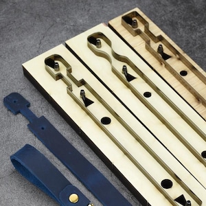 Peut inclure: Des outils de maroquinerie et des lanières de cuir bleues sont présentés. Les outils en métal sont encastrés dans des blocs de bois. Les lanières ont des éléments dorés. L'ensemble est posé sur une surface grise.