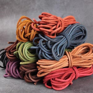 May include: A selection of colourful leather cords in shades of red, orange, green, and blue. The cords are bundled, displaying their texture and colour variations. These cords are suitable for crafting and jewellery making.