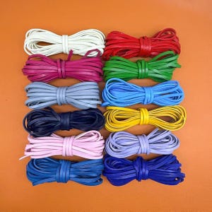 May include: Twelve bundles of flat leather cord arranged in a grid, featuring a variety of colours including white, red, magenta, green, light grey, light blue, dark navy, yellow, light pink, lavender, medium blue, and royal blue.