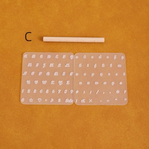 May include: A clear plastic alphabet and number stencil set with a wooden dowel. The stencils include uppercase and lowercase letters, numbers, and symbols. The letter "C" is visible in the upper left corner.
