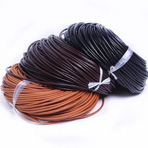May include: Three bundles of leather cord in shades of brown and black, tied with clear plastic and white ribbon. The cords are tightly coiled, with a smooth, glossy finish, and are ready for crafting projects.