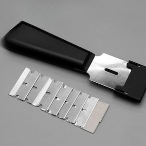 May include: A black handled scraper with a silver blade and a set of replacement blades. The scraper is designed for removing paint, stickers, or other materials from surfaces. The blades are made of steel.