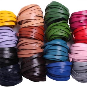 Può includere: Una collezione di strisce di cuoio in vari colori, tra cui giallo, beige, verde e rosa. Le strisce sono arrotolate e impilate, mostrando una gamma di tonalità adatte a progetti di artigianato o design. La pelle appare liscia e flessibile.